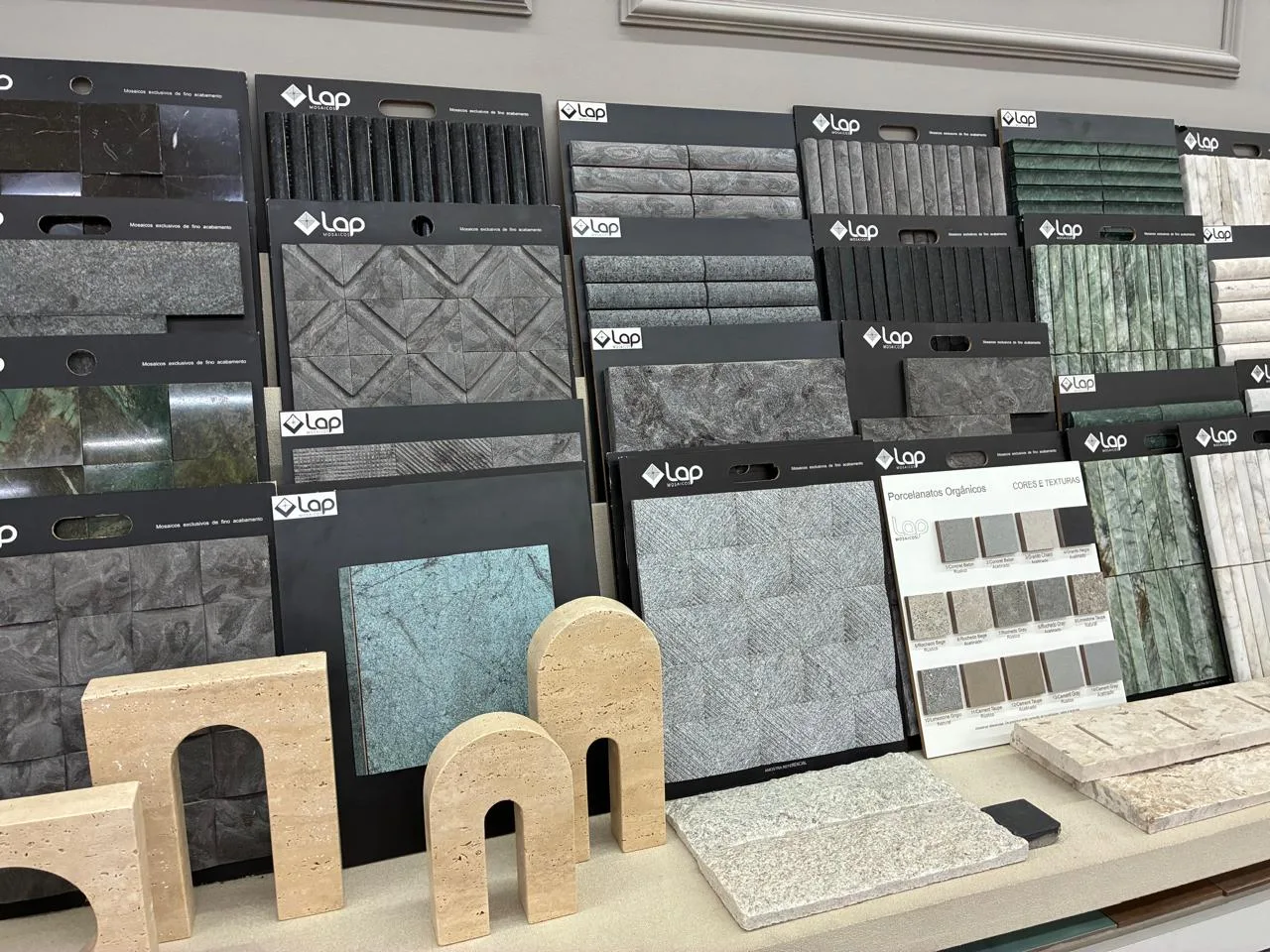Amostras de mosaicos e porcelanatos orgânicos LAP no showroom, com peças em travertino